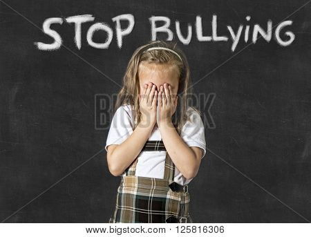 young sweet junior schoolgirl victim of bully crying sad standing in front of school class blackboard with chalk text stop bullying in school children bullied and education stress