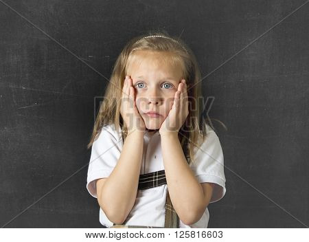 young sweet junior schoolgirl with blonde hair crying sad and shy standing isolated in front of school class blackboard wearing school uniform in children education stress and bullying victim