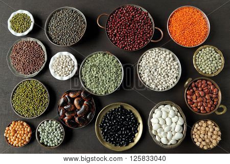 Beans peas and lentils in metal bowls on dark background.