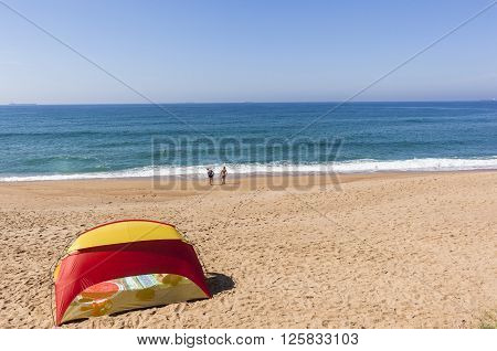 Beach tent blue ocean horizon with holiday bathers swimming coastline landscape.