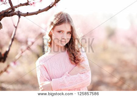 Beautiful blonde teenage girl 14-16 year old posing in peach garden. Looking at camera. Elegance.