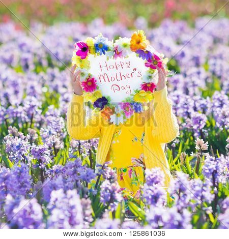Child playing in hyacinth field. Little girl holding a wooden heart shape chalk board standing in a park with spring hyacinths flowers. Copy space for your text. Happy mother's day card.