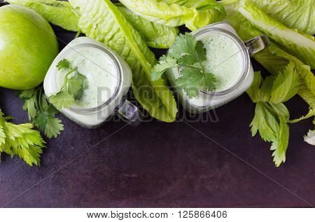 Two glasses of green smoothie and fresh green vegetables and fruits on black background. Top view