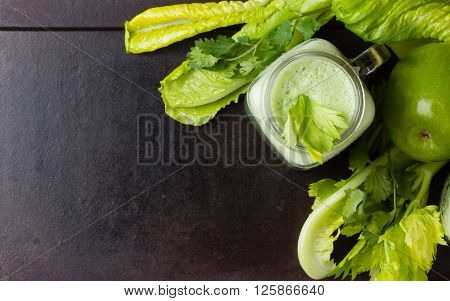Glass of green smoothie and fresh green vegetables and fruits on black background. Top view