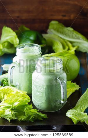 Two glasses of green smoothie and fresh green vegetables and fruits on wooden blue background