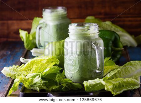 Two glasses of green smoothie and fresh green vegetables and fruits on wooden blue background