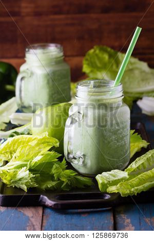 Two glasses of green smoothie and fresh green vegetables and fruits on wooden blue background