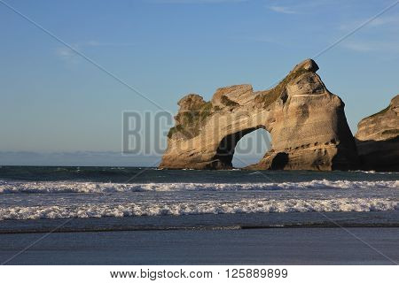 Unique rock formation at Wharariki Beach. Island with big hole. Beautiful scenery at the west coast of the South Island.