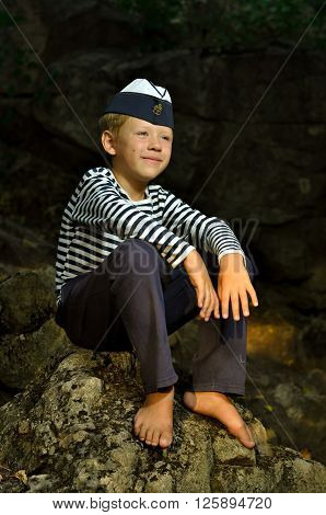 boy in a frock and garrison cap sitting on the stone with barefooted