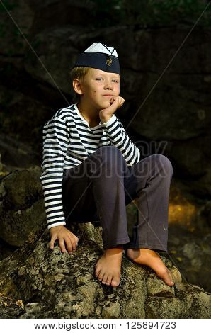 boy in a frock and garrison cap sitting on the stone with barefooted