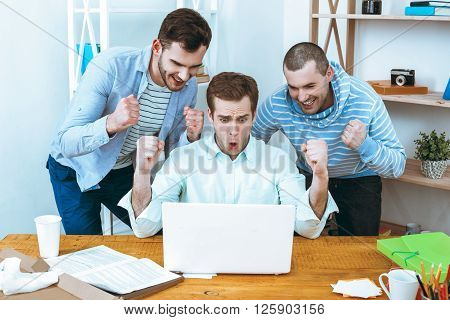 IT company. Young programmers working with laptop. Nice office interior. Professional coders looking at laptop and rejoicing