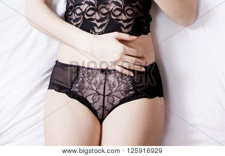 Sexy girl in black lace panties and top lying on the bed, hand on belly, no face, anonymous, body detail