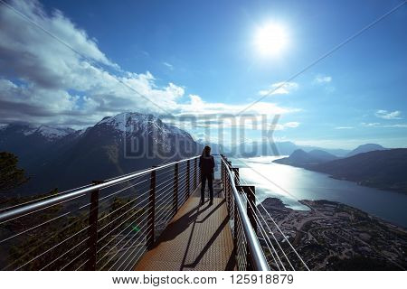 girl hiker with a backpack standing on viewing platform and looking on Romsdalsfjorden and Andalsnes Norway