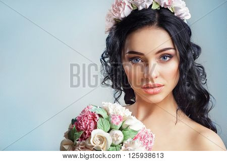 Beautiful young girl with a floral ornament in her hair on a blue background.Portrait of a beautiful woman in a wedding dress in the image of the bride. Picture taken in the studio. Portrait of beautiful bride. Wedding dress. Wedding decoration