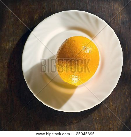 Ripe orange in white plate on wooden background