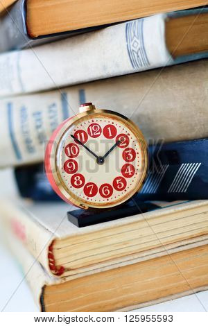analog retro red alarm clock on a heap of old books