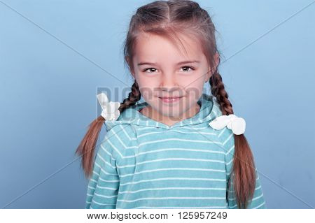 Smiling cute girl 3-4 year old posing over blue. Looking at camera. Wearing blue striped hoodie.