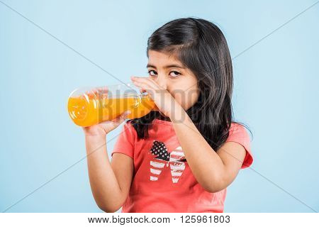 indian girl with cold drink bottle, asian girl drinking cold drink in pet bottle, girl kid and cold drink, indian cute girl with mango or orange cold drink in plastic bottle, isolated on blue