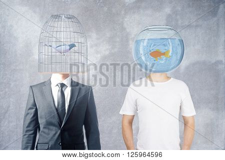 Businessman and casually dressed man with fishtank and birdcage instead of heads on concrete background