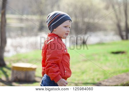 Close up portrait of a beautiful baby boy walking in spring park. Little boy in orange jaket and blue jeans, outdoors
