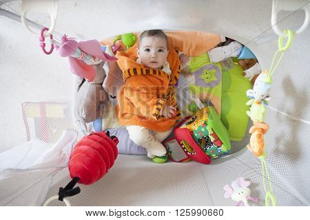 Cute baby girl at playpen full of soft toys. 8 months old