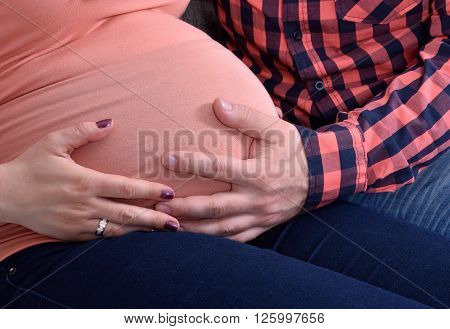 Young couple expecting a baby. Husband holding hand on his pregnant wife's stomach.