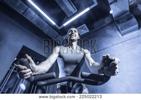 The Guy Is Engaged In A Bicycle Simulator In The Gym. Toned Image.