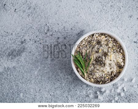 Sea salt scented herb rosemary and lemon zest. Sea salt with aromatic herbin small bowl on gray cement background. Scented salt and ingerdients. Copy space. Top view or flat lay
