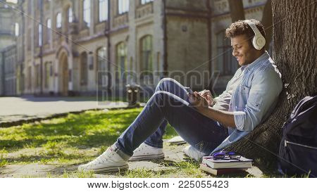 Young Male In Headphones Sitting On Grass, Leaning Against Tree, Choosing Song, Stock Footage