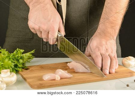 Chicken making. A man in an apron is cutting meat on a wooden board. Preparation of healthy food.