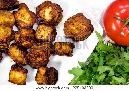 Close-up image of a delicious ghee, fried Indian cottage cheese slices on a plate with tomato and rocula