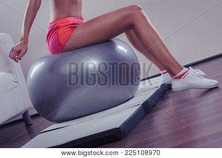 Sport, training, gym and lifestyle concept. Young attractive slim woman in sportswear doing fitness exercises with fit ball at home