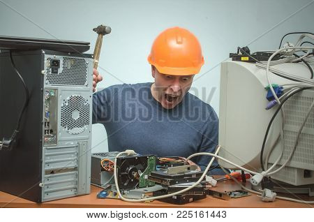 Enraged computer technician man is screaming and breaks a PC by hammer. PC repair service center. Mad system administrator in stress overburdened by work.