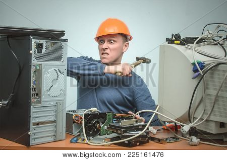 Enraged computer technician man is screaming and breaks a PC by hammer. PC repair service center. Mad system administrator in stress overburdened by work.