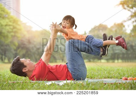 Happy young Asian father and his daughter lying on the grass and playing together in nature at park outdoor. Family Having fun.