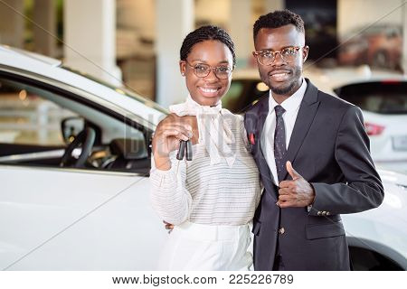 Visiting Car Dealership. Beautiful African Couple Is Holding A Key Of Their New Car, Looking At Came
