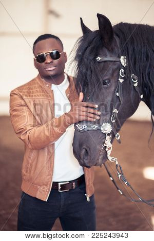 African Man Wearing Sunglasses Near A Black Horse In Hangar