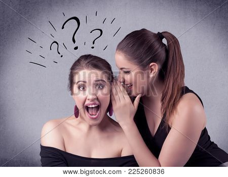 A teenager girl looking confused with drawn question marks above the head, while a girlfriend whispers something in her ear concept.
