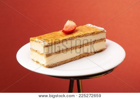 Milfey napoleon cake with fresh strawberries. Piece of layered cake with pastry cream custard on white plate on cake board, close-up. Delicious homemade dessert.