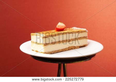 Milfey napoleon cake with fresh strawberries. Piece of layered cake with pastry cream custard on white plate on cake board, close-up. Delicious homemade dessert.
