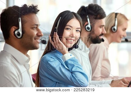 Young cheerful beautiful business woman in headset. Smiling female asian customer service representative looking at the camera.