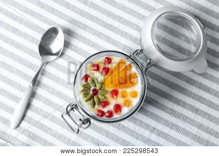Yogurt with date plum, pomegranate and pumpkin seeds in jar on fabric