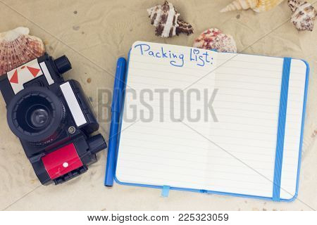 Enjoying vacation planning mood, notepad and vintage camera on white sand background. Top view, closeup.