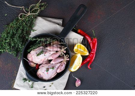 Small raw quals with some spice ready for cooking on black round pan .