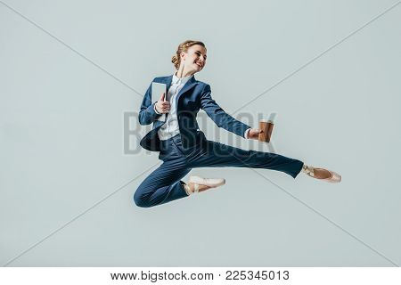 Businesswoman In Suit And Ballet Shoes Jumping With Coffee And Digital Tablet, Isolated On Grey