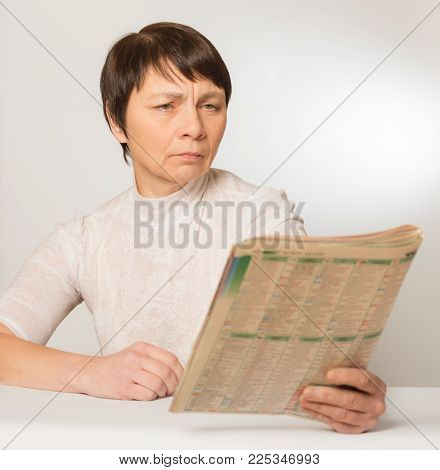 Presbyopia, vision problems. An elderly woman without glasses reads a newspaper pushing her away