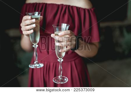 girl in a pomegranate dress and with french manicure holding in her hands two glasses with champagne. Noface