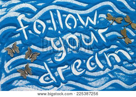 Follow Your Dream On A Blue Colored Sand With Waves And Decorations, Top View, Flat Lay