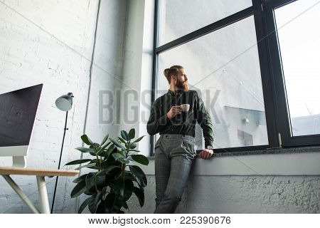 Bottom View Of Bearded Businessman Standing With Cup Of Coffee And Looking At Window