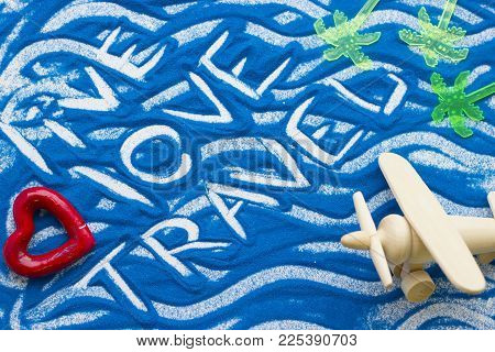 Live Love Travel Inscription On A Blue Colored Sand With Waves, Plastic Palm Trees And Toy Wooden Pl